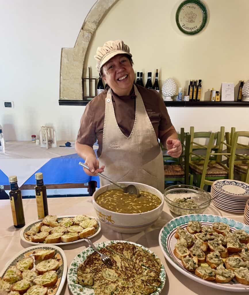 Kok serverer suppe med brødretter på bordet.