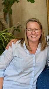 Smilende kvinde i lyseblå skjorte sidder indendørs.