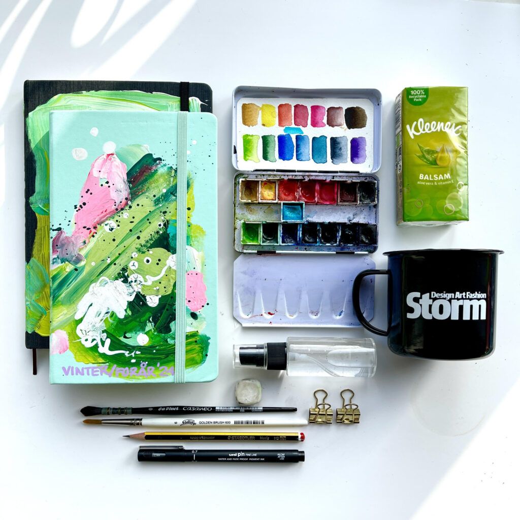 Malerredskaber og notesbøger på et bord.